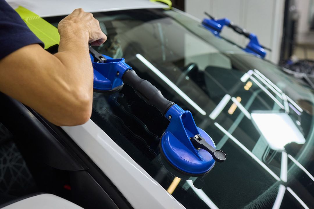 Persona que utiliza ventosas azules para instalar el parabrisas de un coche.
