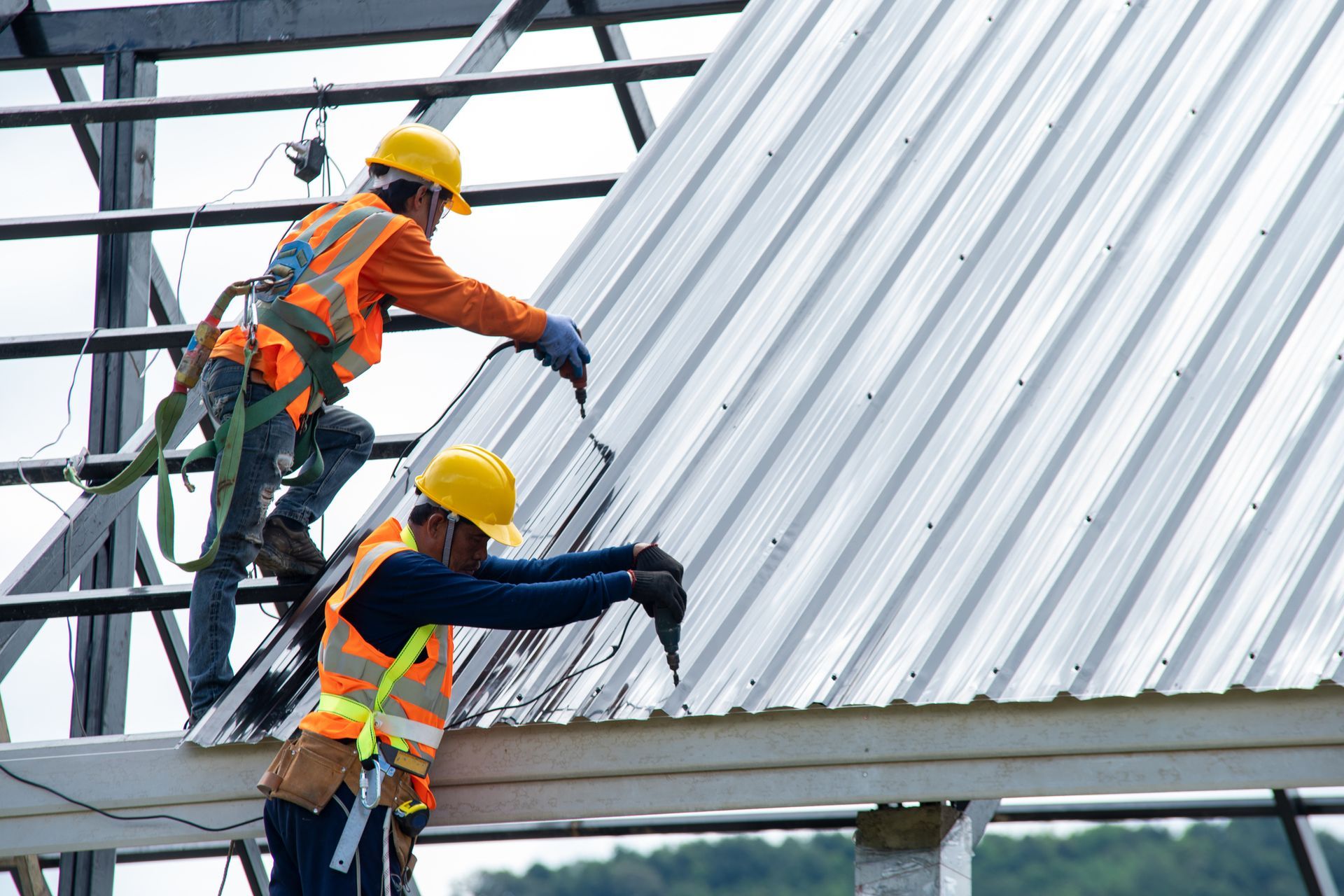 Two construction workers are working on a metal roof.