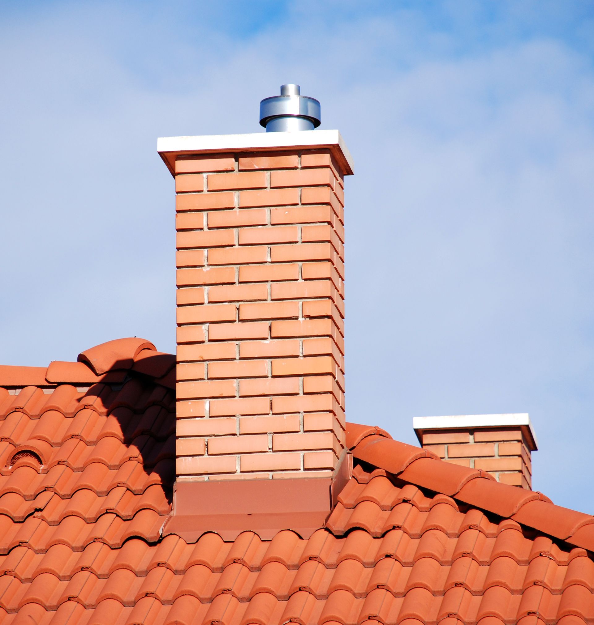 A brick chimney on top of a red tiled roof