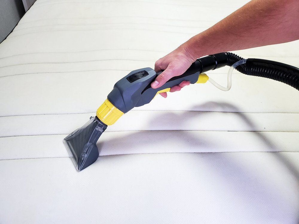 A Person Cleaning a White Mattress with A Handheld Upholstery Cleaner — Les's Eco Carpet Cleaning in Bangalow, NSW