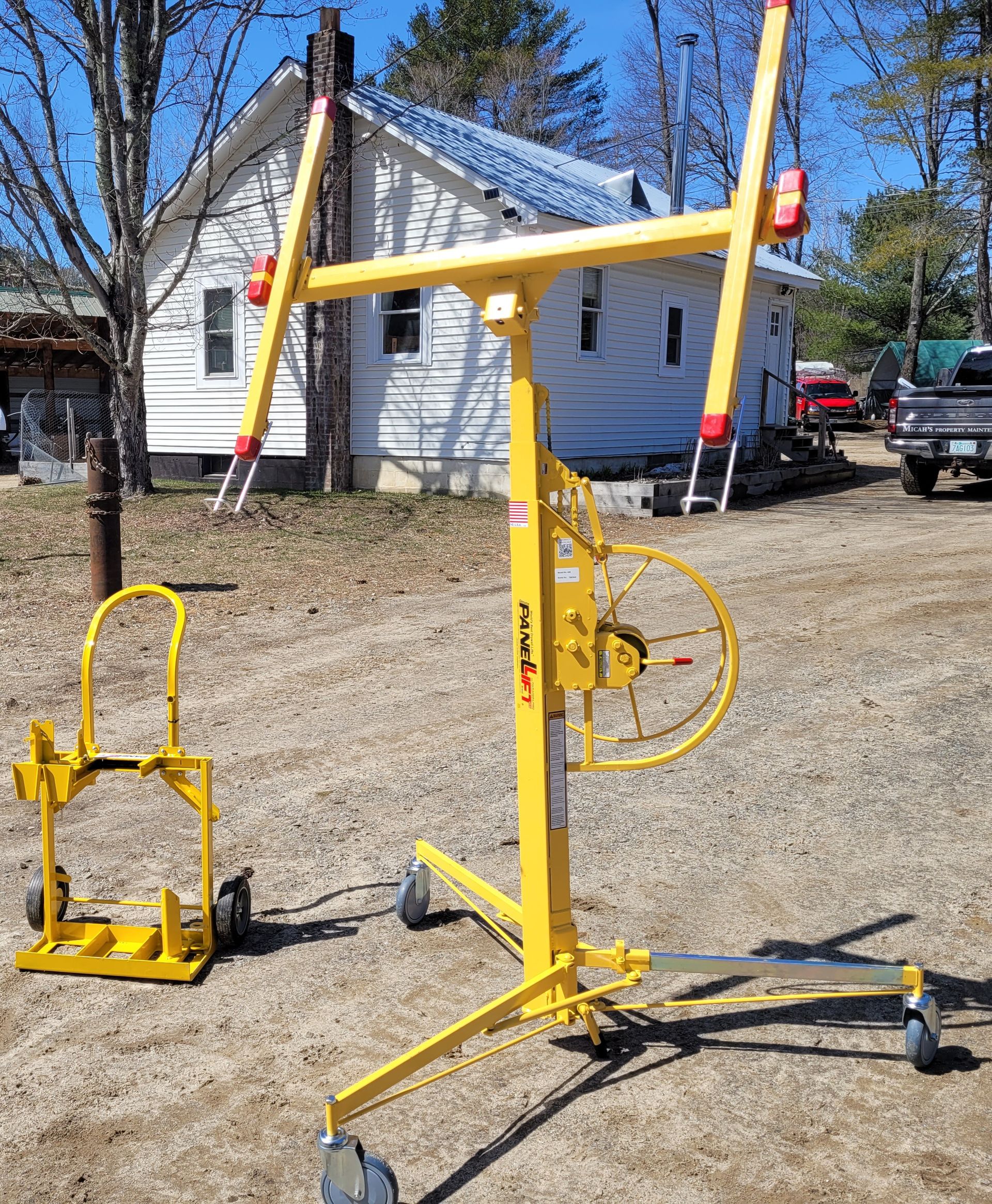 A yellow lift is sitting in the dirt in front of a house.