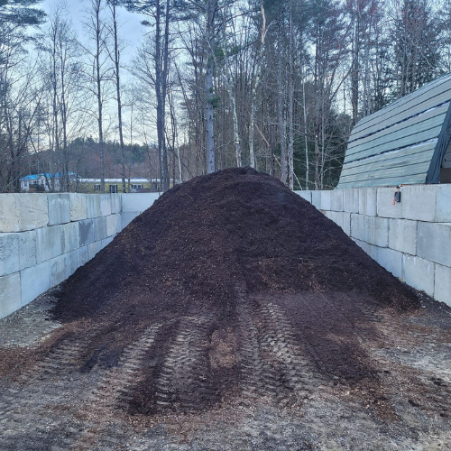A large pile of dirt is sitting in front of a brick wall.