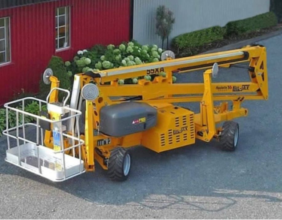 A yellow boom lift is parked in front of a red building