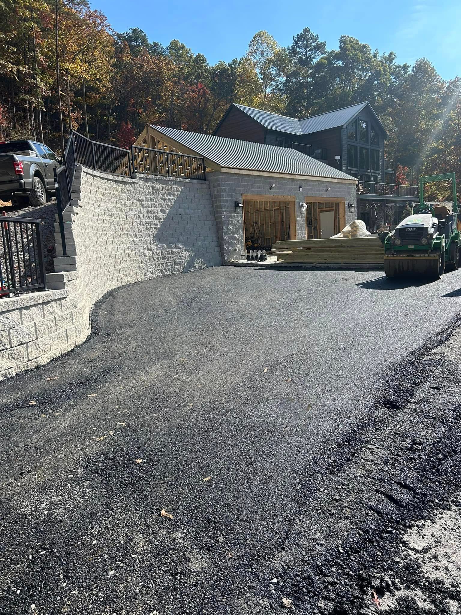 Gravel driveway leading to a stone building with an open-air carport under construction. Wood and green tractor visible.