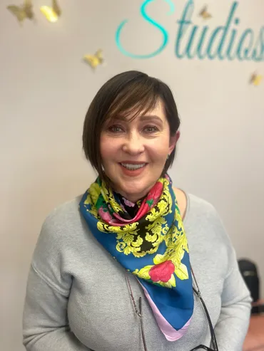 Woman in grey sweater and patterned scarf smiles in front of