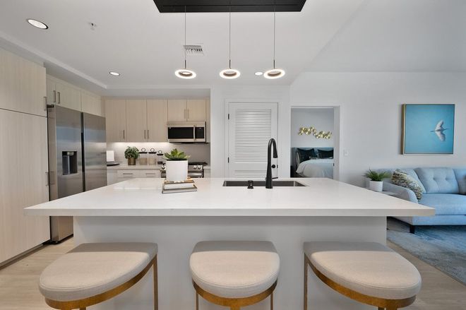 Modern kitchen with white countertops, light wood cabinets, island with stools, and open to living area.