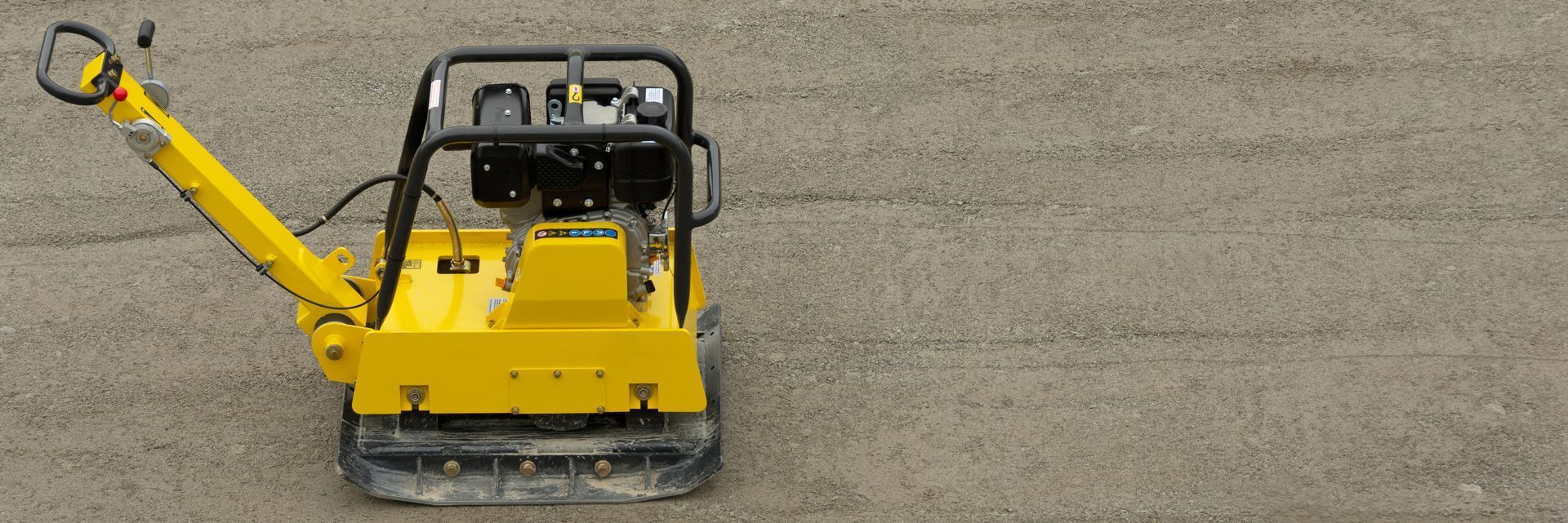 Máquina de construcción amarilla con ruedas y brazo elevado sobre una superficie de grava.