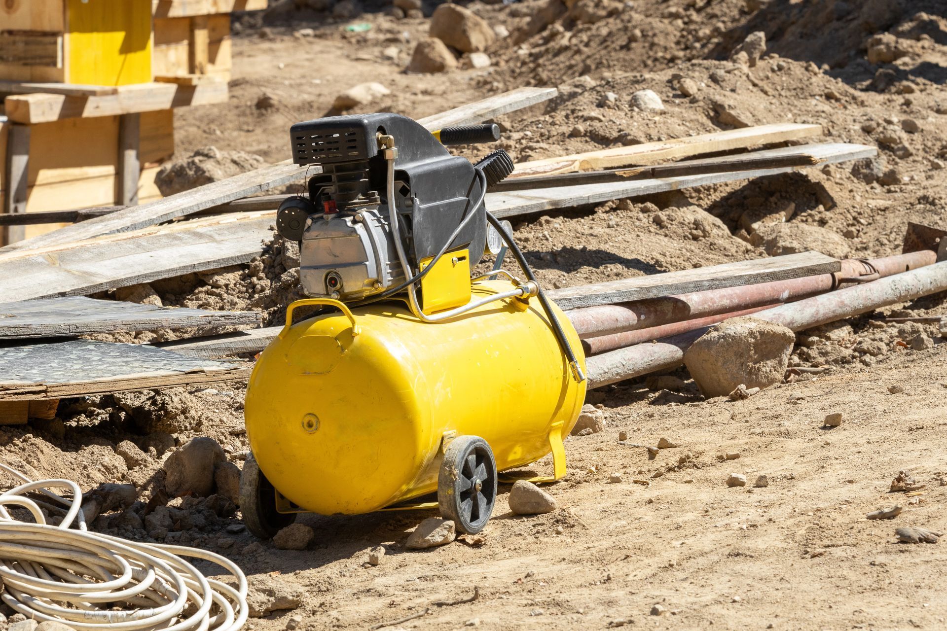 Compresor de aire amarillo en una obra en construcción polvorienta con tuberías y madera esparcidas.