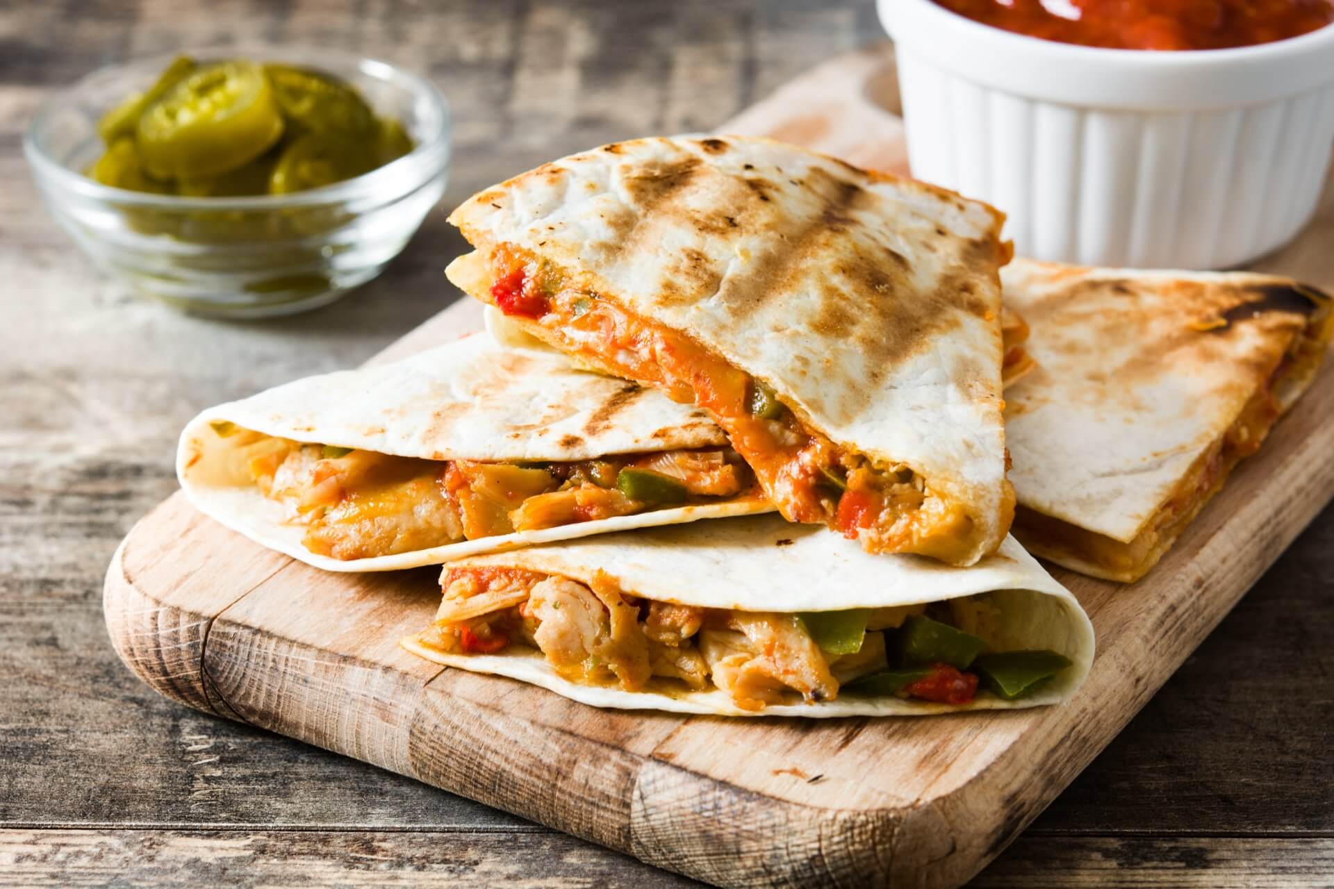 the quesadillas are stacked on top of each other on a wooden cutting board .