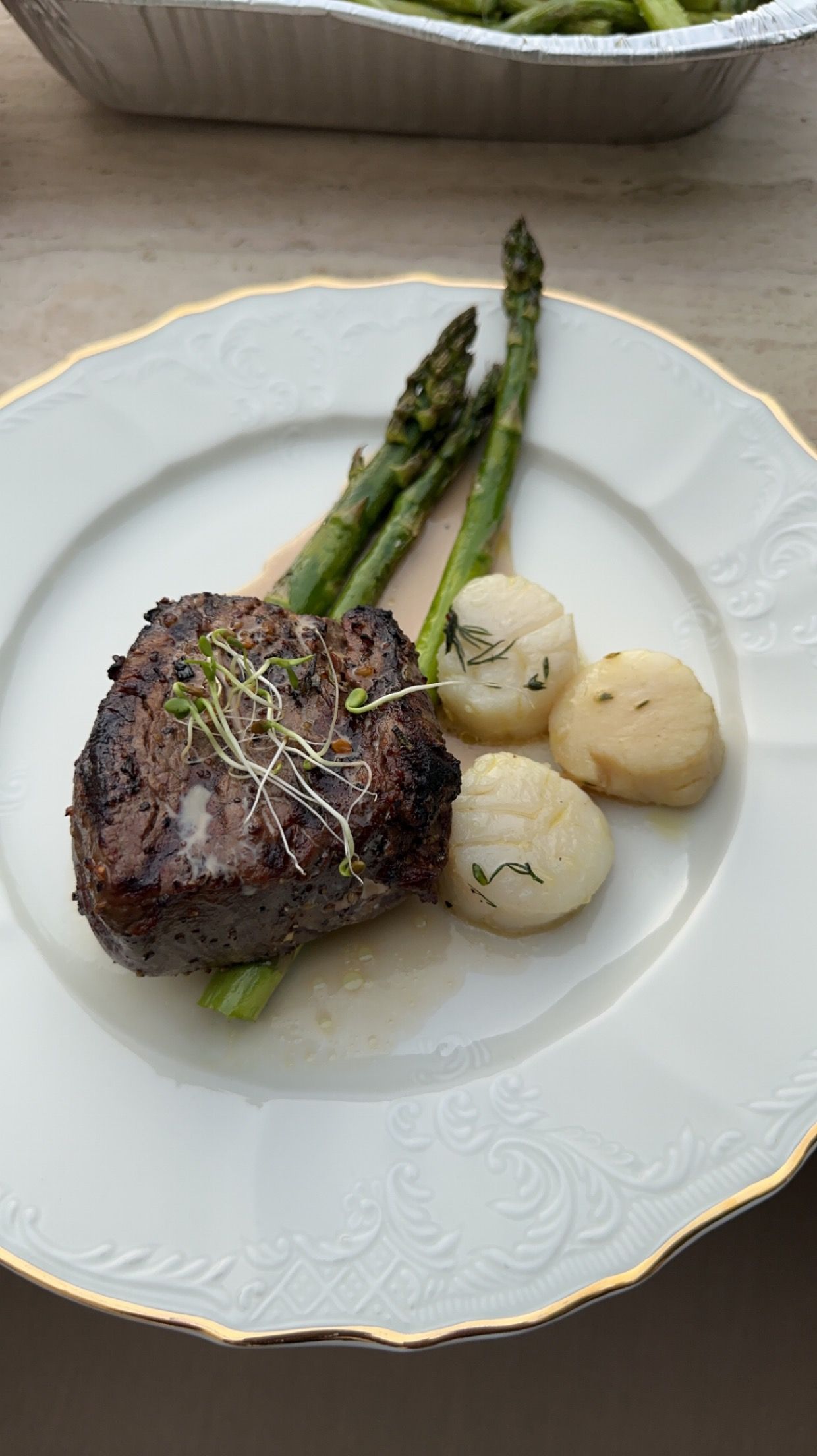 A white plate topped with a steak asparagus and scallops