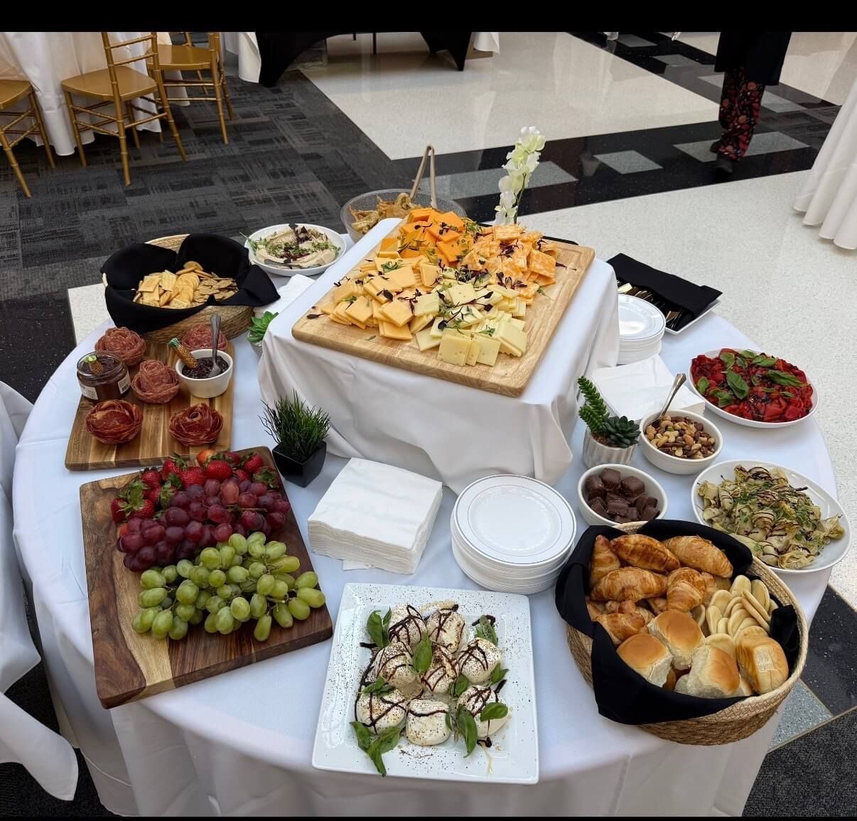 Buffet table with pastries, fruit, salads, and finger foods on white tablecloths at an indoor event