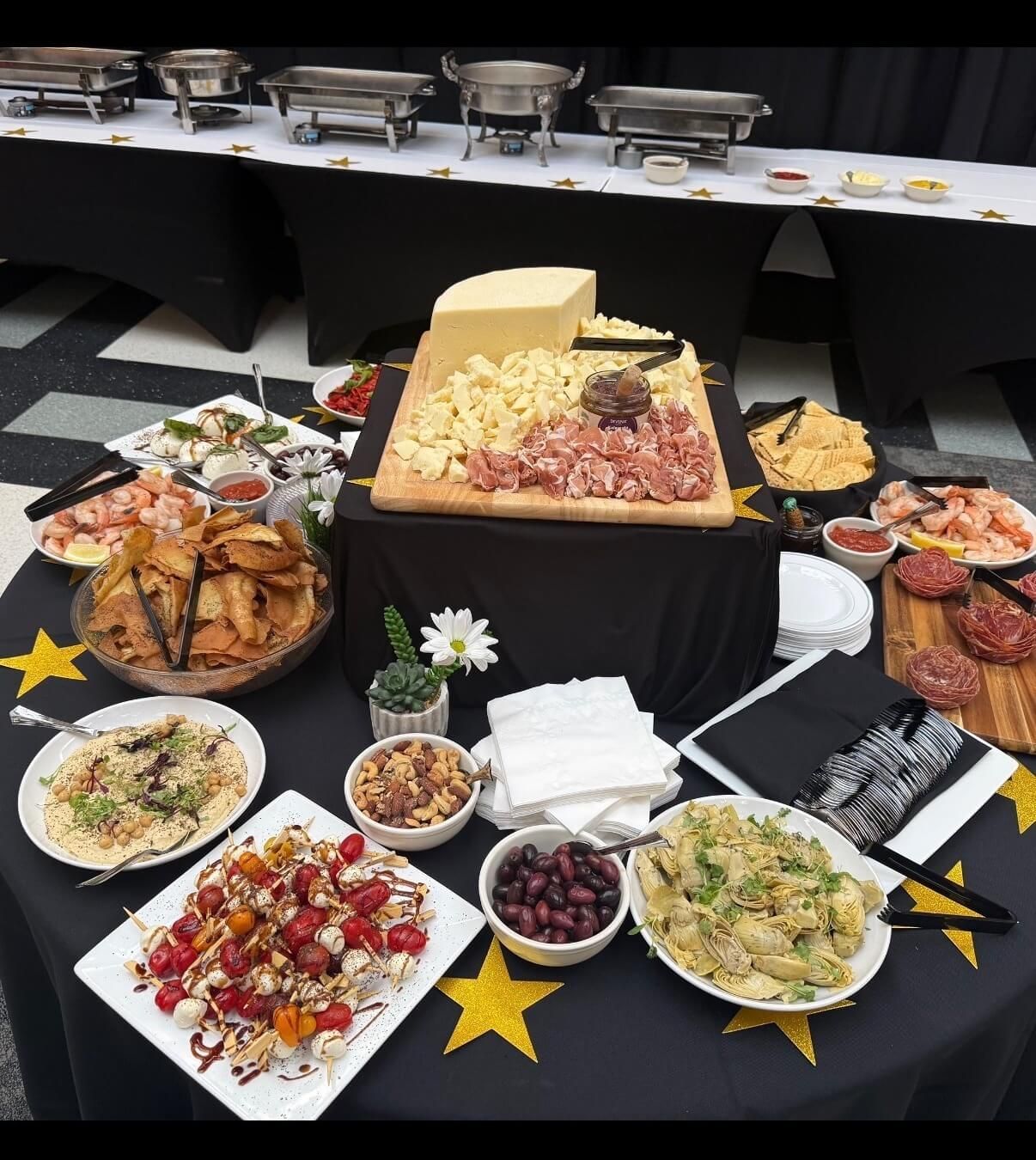 Buffet table with assorted foods, including charcuterie, salads, dips, and a large cheese wheel centerpiece