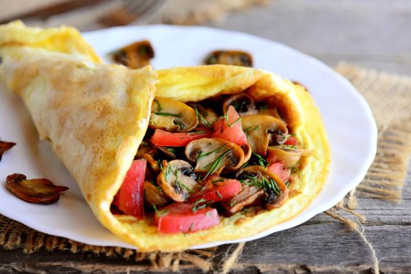 a close up of an omelet with mushrooms and tomatoes on a plate .
