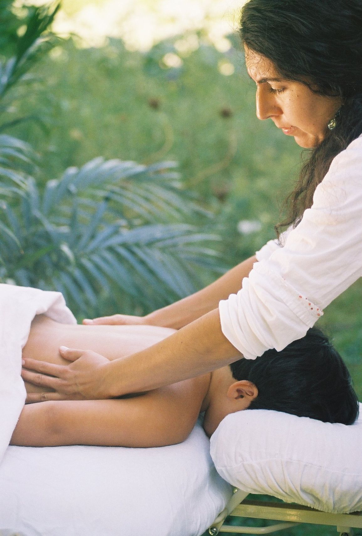 A woman is giving a man a massage on a table outside.