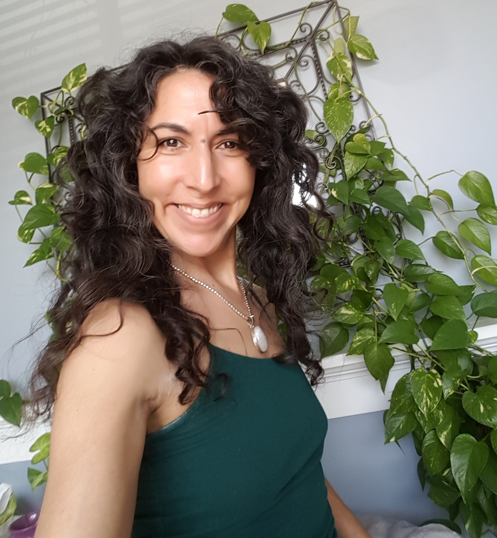 A woman with curly hair is smiling in front of a plant.