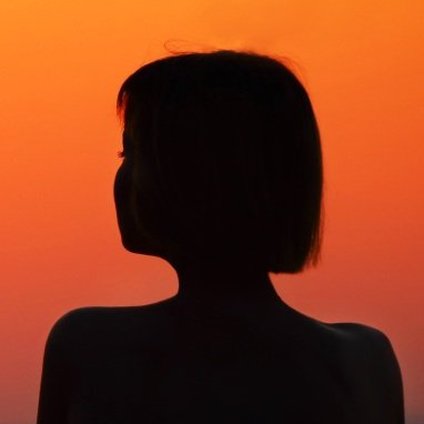 A silhouette of a woman 's back with a sunset in the background.