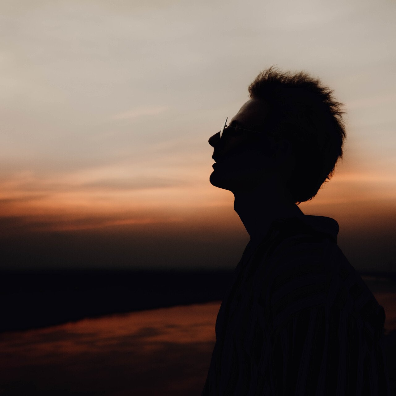 A silhouette of a man looking up at the sky at sunset.