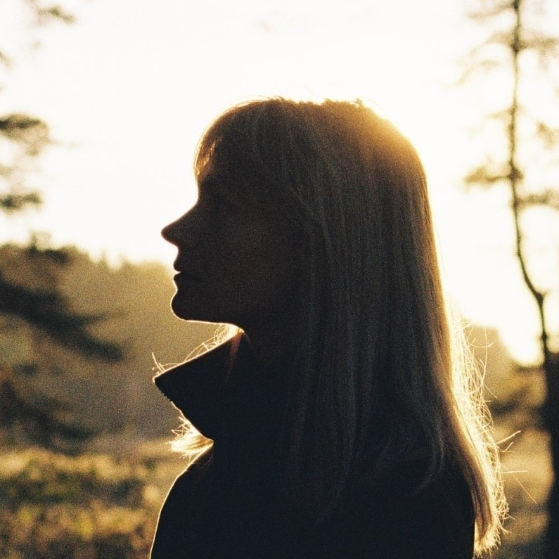 A silhouette of a woman in a field with trees in the background