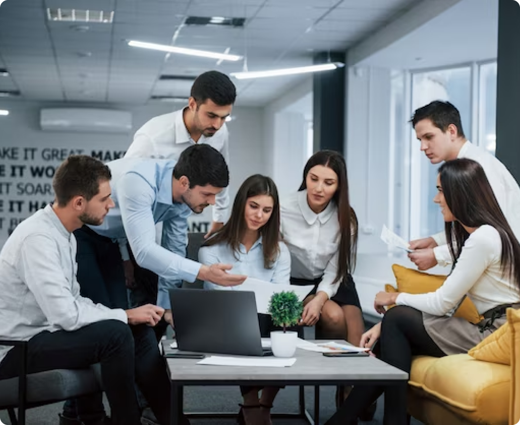 A group of people are sitting around a table looking at a laptop.