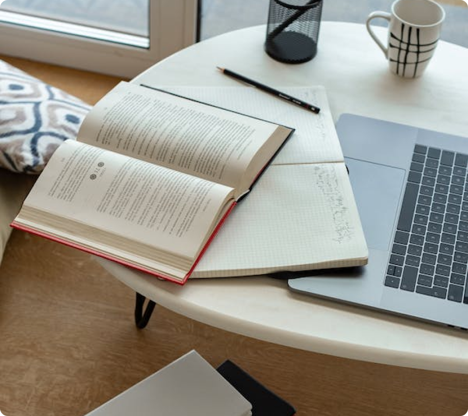 A book is open on a table next to a laptop