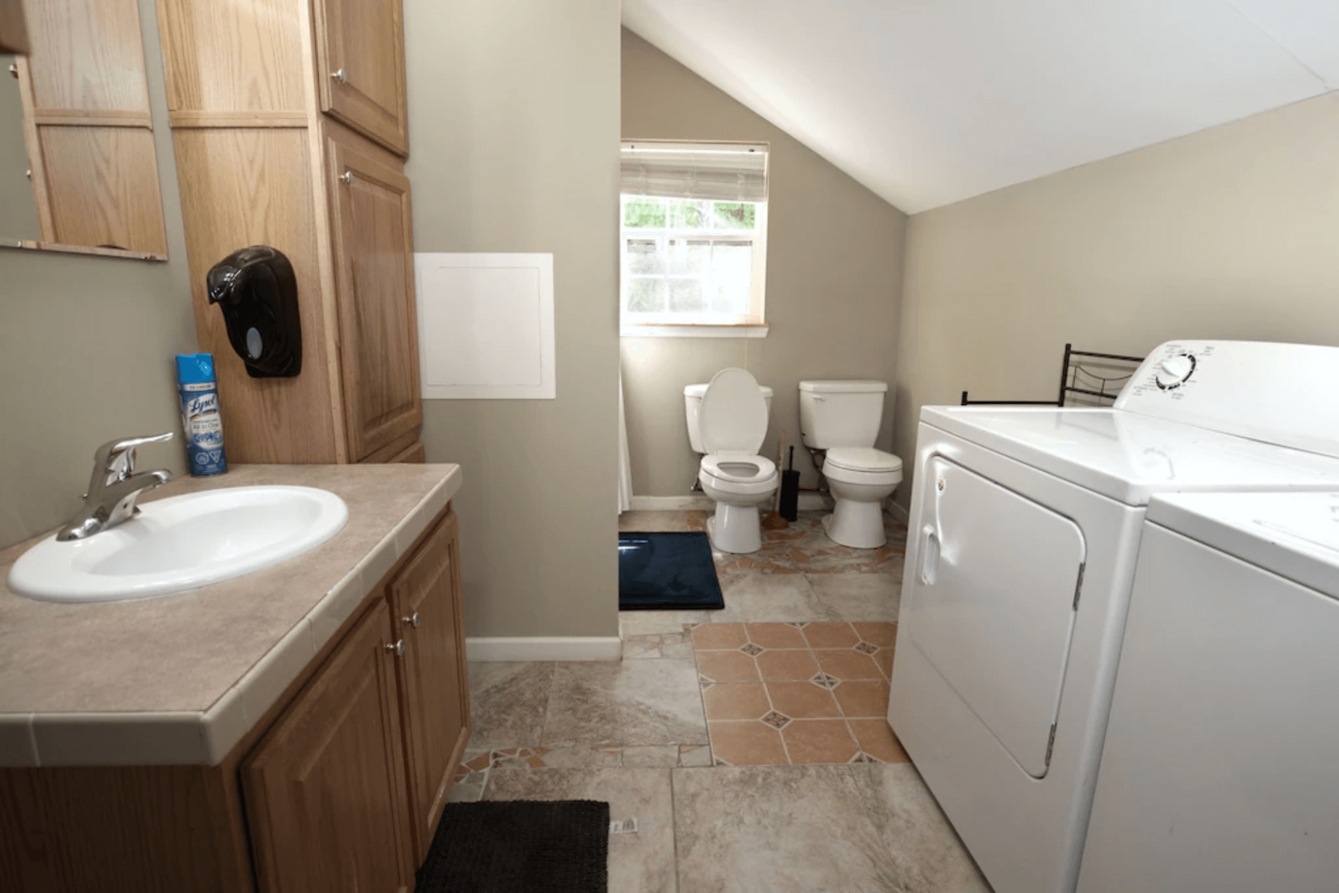 A bathroom with a sink , washer and dryer , toilet and mirror.