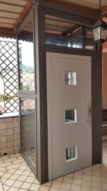 Una cabina di accesso grigia con tre finestrelle, situata su un patio esterno pavimentato, sotto una struttura coperta