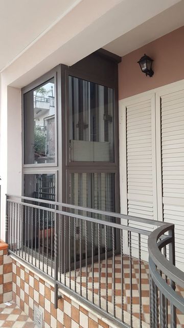 Balcone con ringhiera in metallo, pavimento a piastrelle a scacchi, porta a vetri e persiane bianche a lamelle