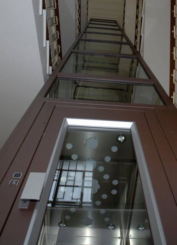 Guardando verso l’alto in un vano ascensore di vetro con struttura marrone e decorazioni a puntini satinati sulle porte.