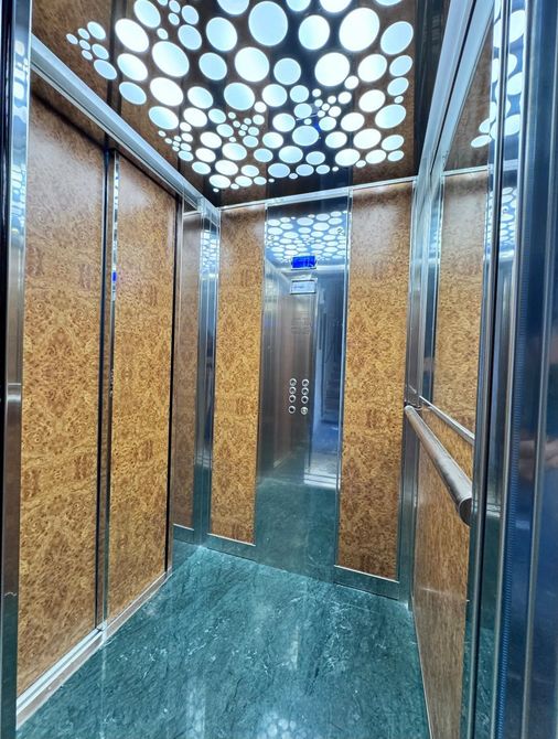 Interno di ascensore vuoto, con pareti metalliche, pavimento color ottanio e un motivo di luci puntiformi sul soffitto