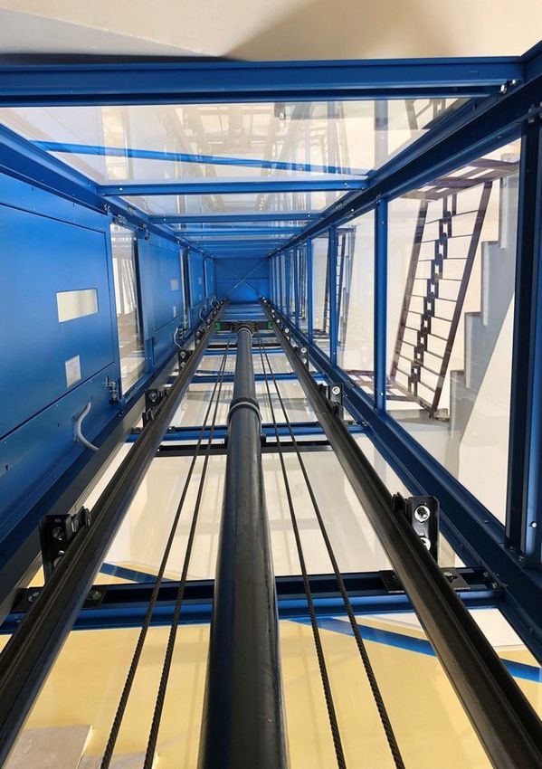 Vista verso l’alto all’interno di un vano ascensore industriale blu, con guide e scala a vista