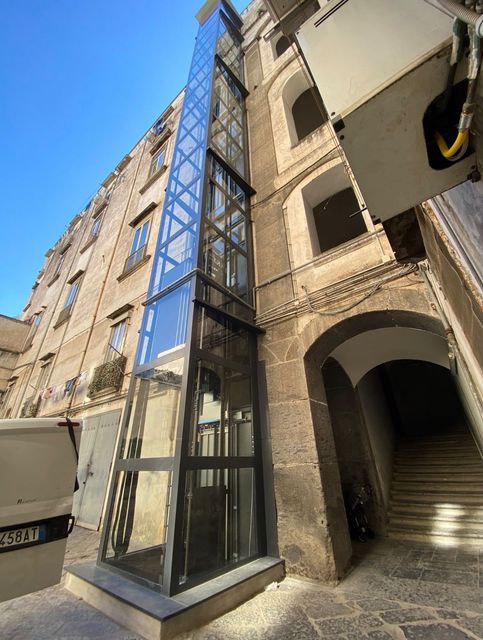 Moderno condominio con ascensore panoramico in vetro e ingresso ad arco sotto un cielo azzurro