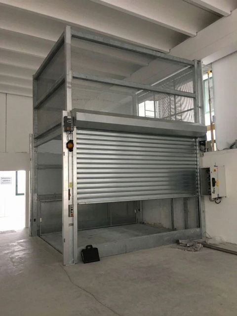 Baia di carico industriale con portone avvolgibile metallico sollevato all’interno di un magazzino.