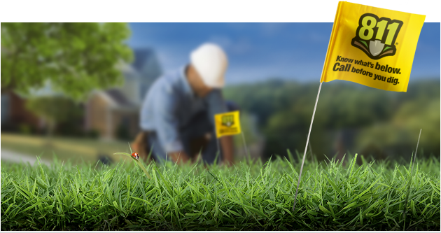 Yellow 811 flag in grass with worker kneeling in background.