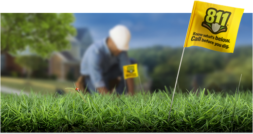 Yellow 811 flag in grass with worker kneeling in background.