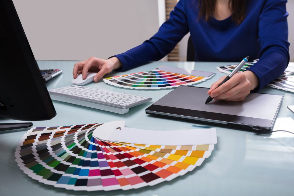 Designer selecting colors from swatches at a desk with laptop and notebook