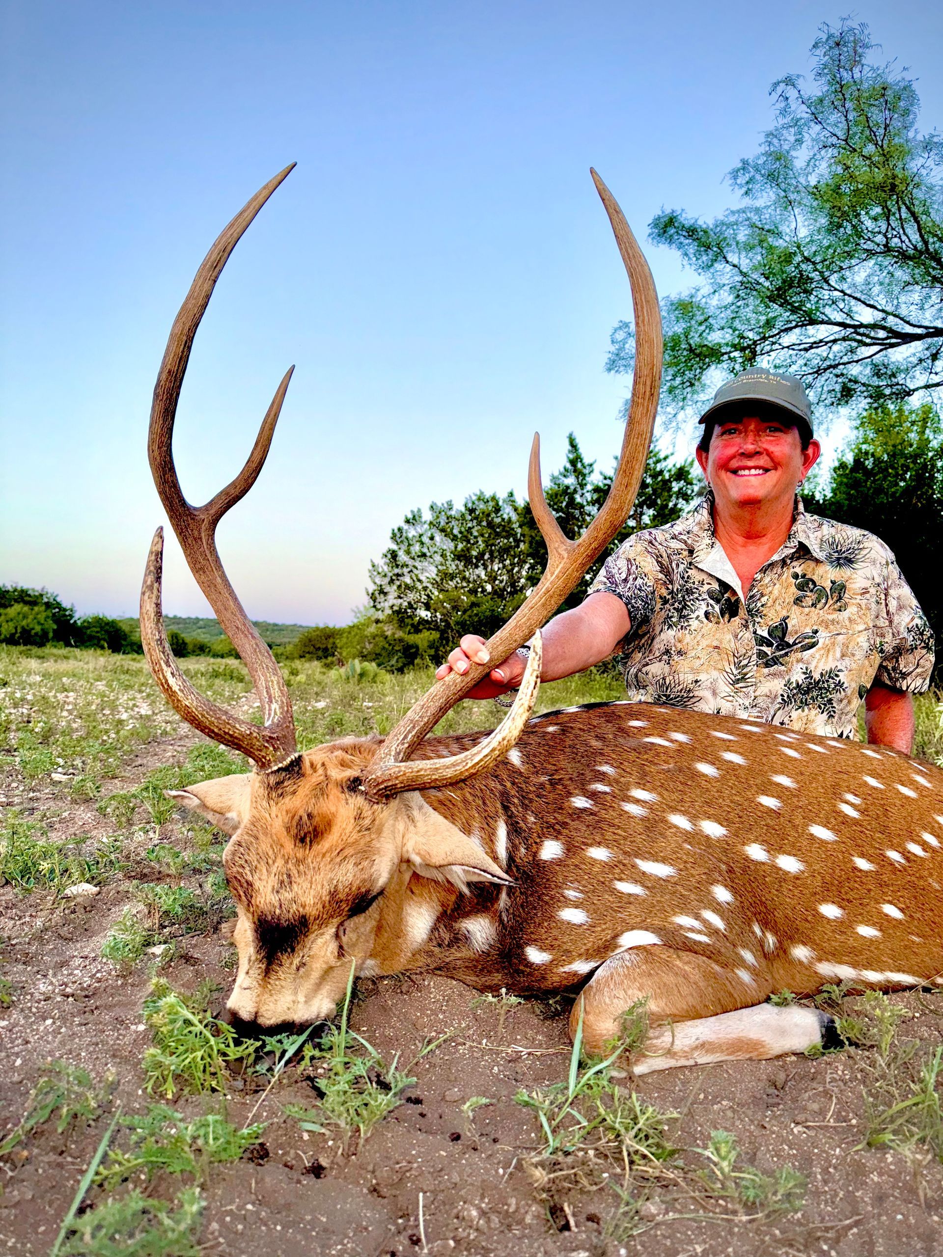 Hunter with a spotted deer and large antlers, posed outdoors on a sunny day.