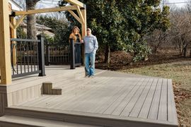 A spacious outdoor patio with a stone fireplace, wicker furniture, and tall tables under a covered roof.