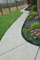 A narrow stone walkway flanked by concrete planter boxes and hedge rows with gravel strips on both sides.
