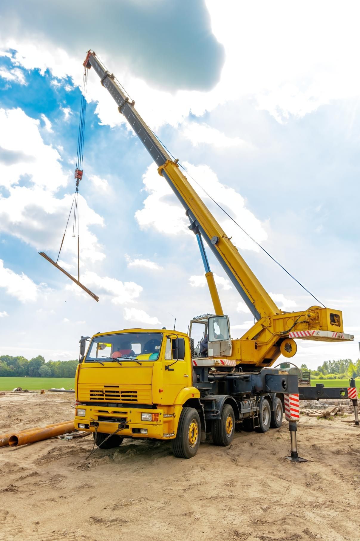 Yellow crane lifting a beam at a construction site under a cloudy sky.