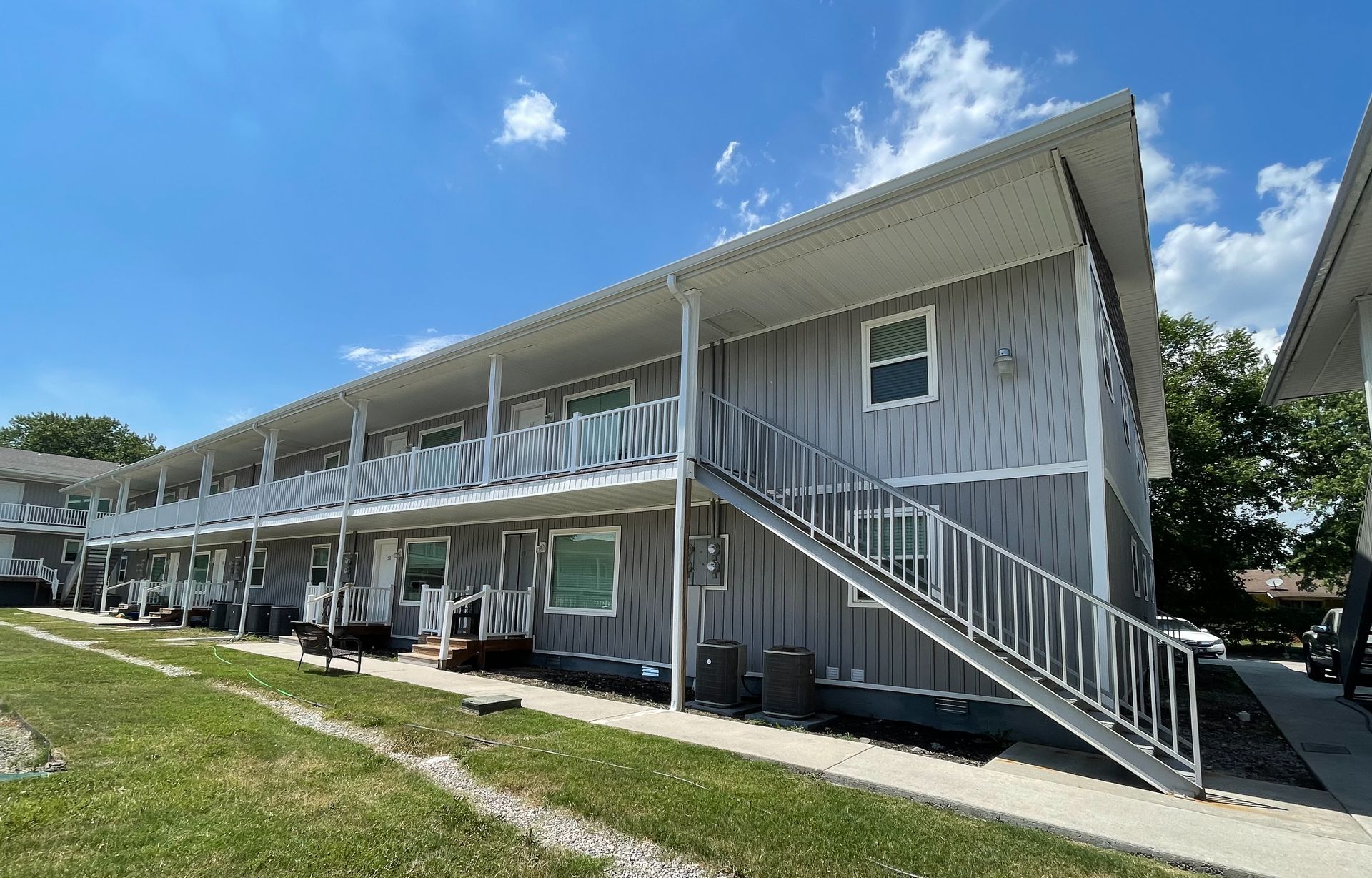 Two-story gray apartment building with exterior staircases under a bright blue sky