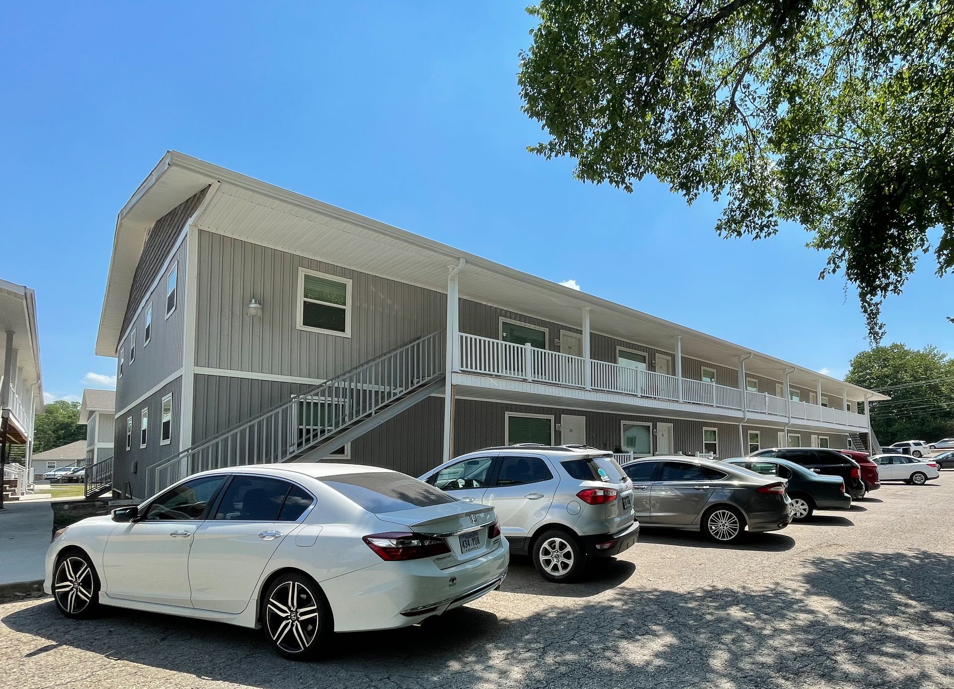Two-story motel with parked cars under a bright blue sky and tree shade