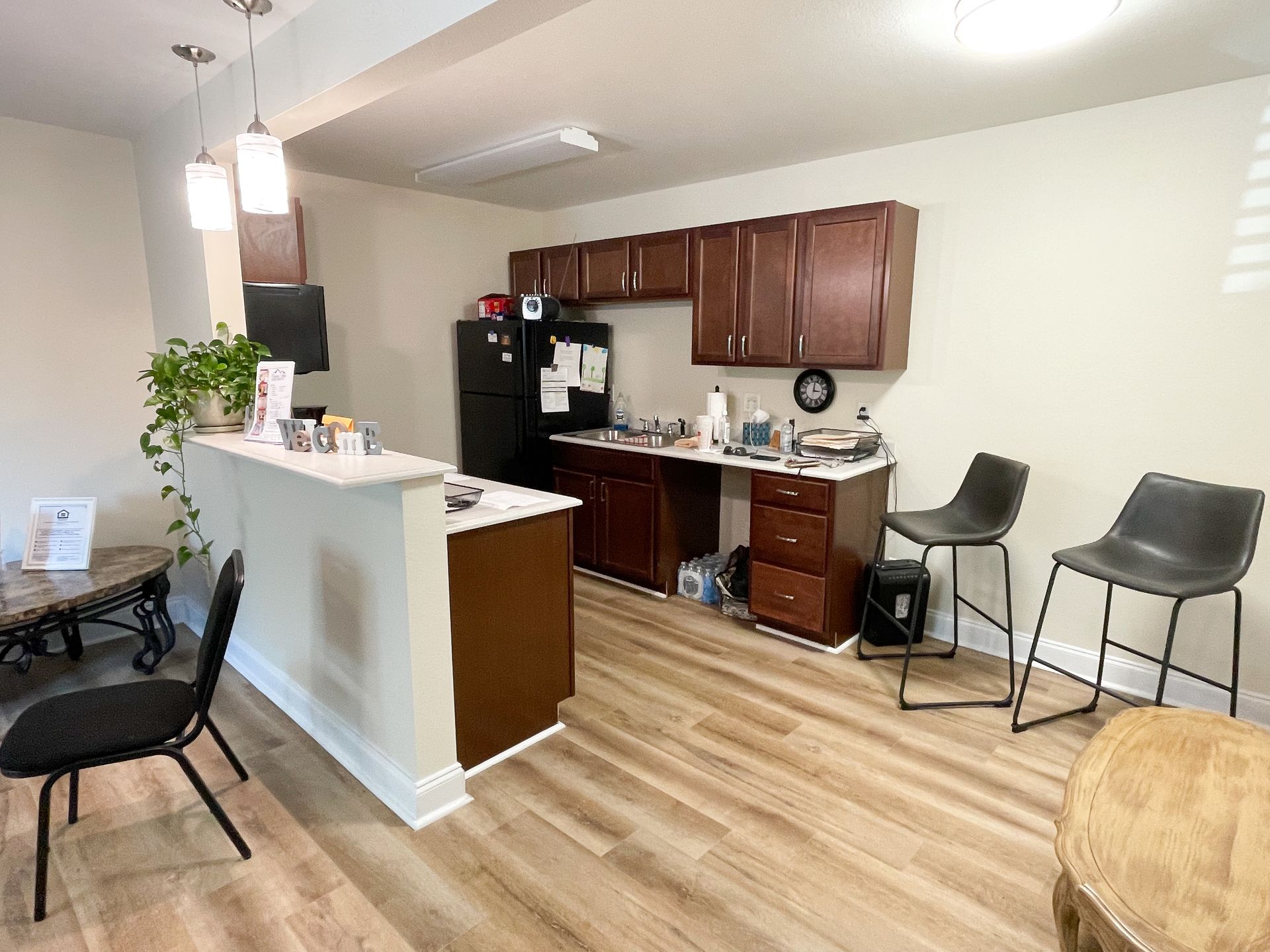 Open kitchen and dining area with wood cabinets, black appliances, and bar stools on a light wood floor.