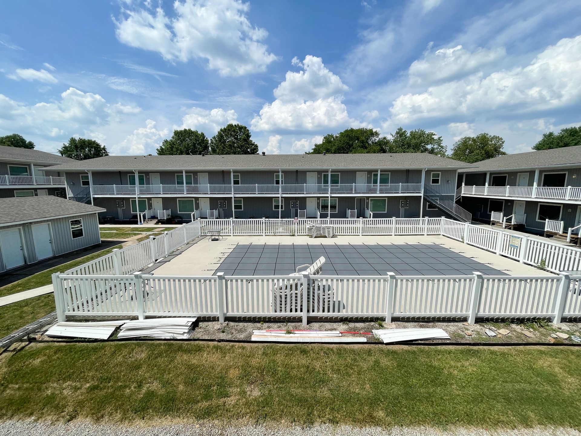 Outdoor swimming pool with white fence, lounge chairs, and a two-story motel under a blue sky