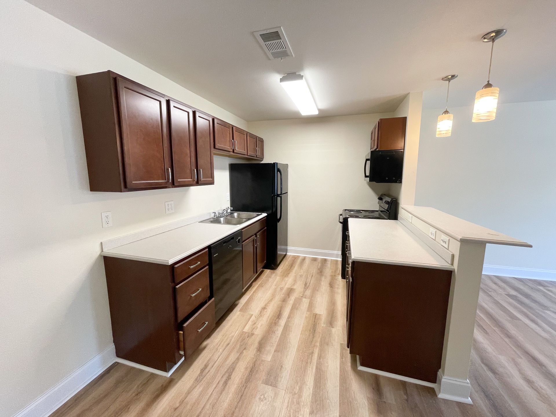 Empty modern kitchen with dark cabinets, light countertops, and wood-look flooring
