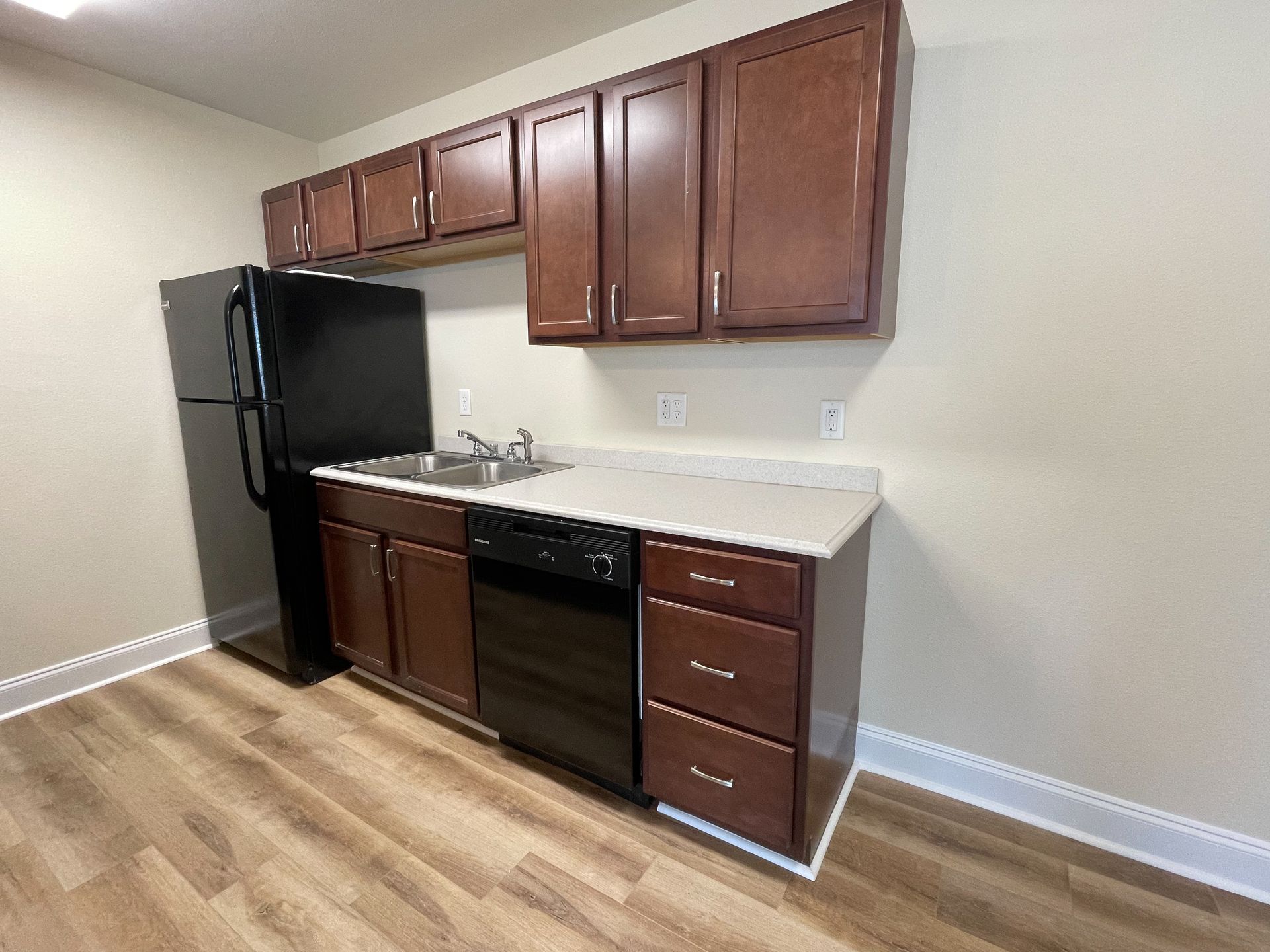 Small kitchen with black refrigerator and stove, brown cabinets, and white countertops.