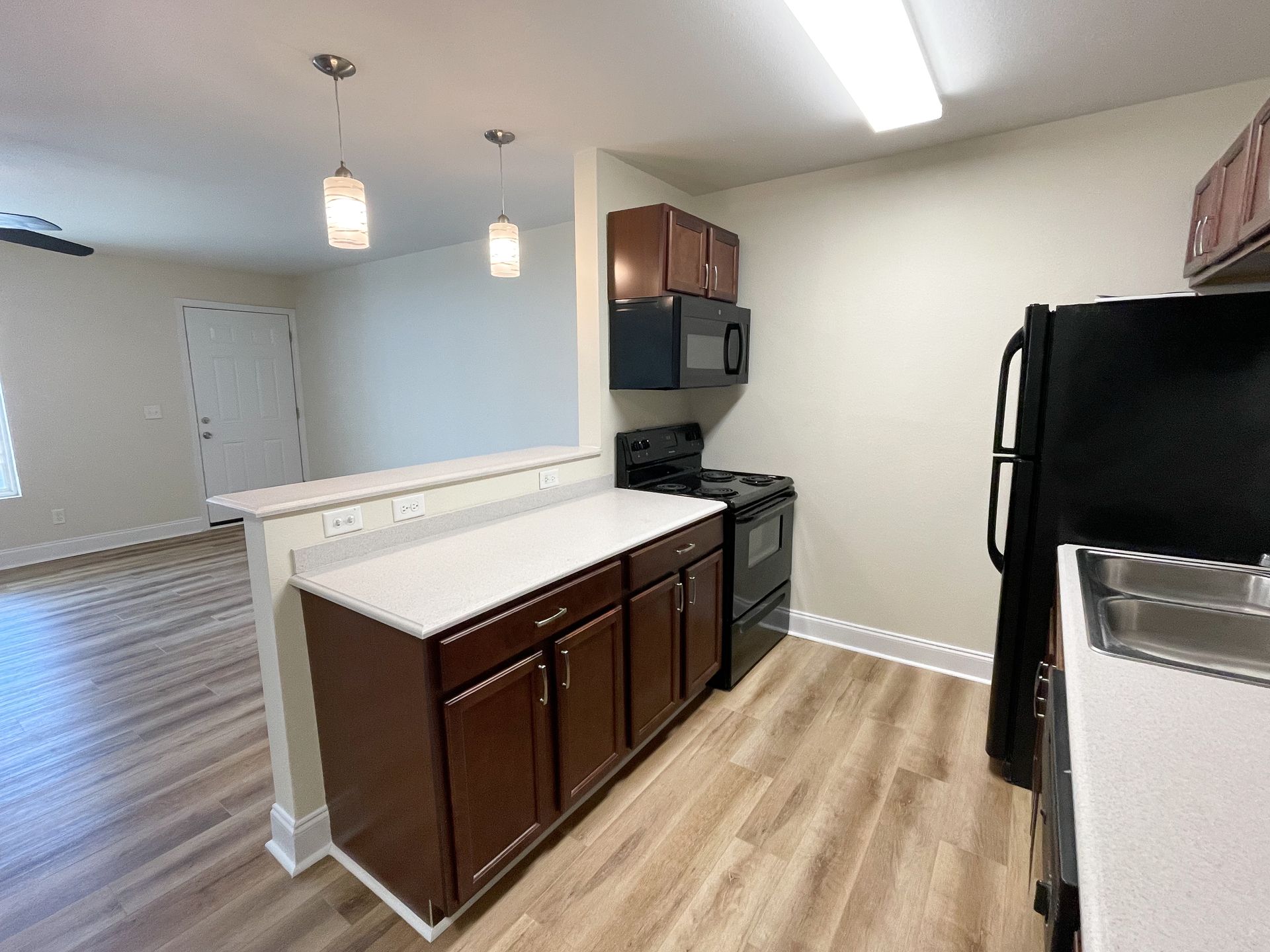 Modern kitchen with dark wood cabinets, white countertops, black appliances, and light wood flooring.