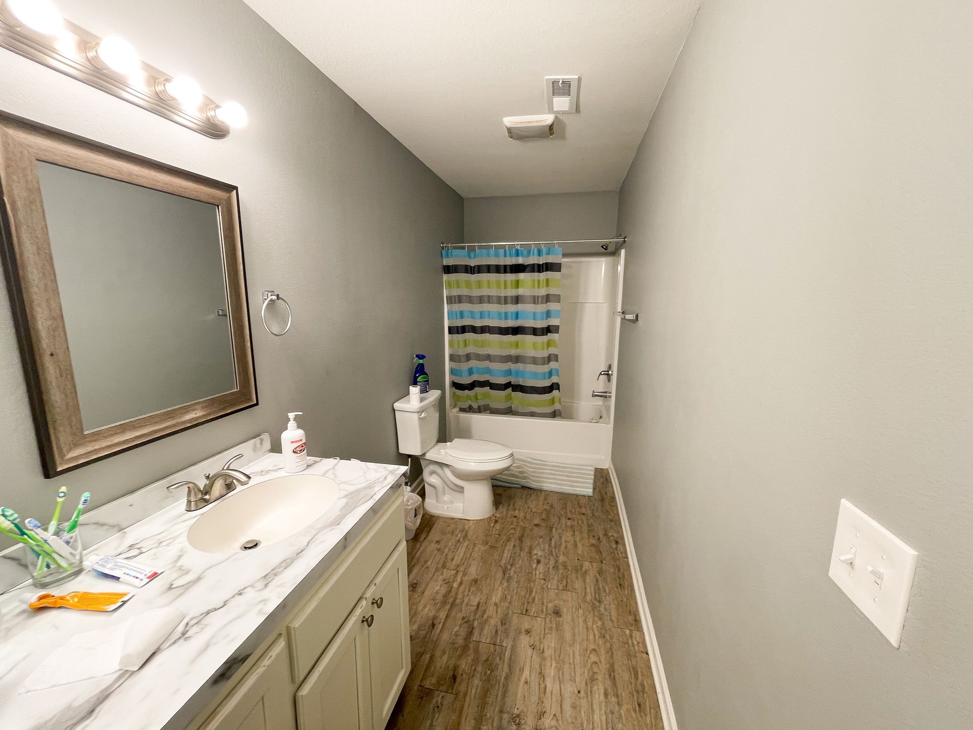 Narrow bathroom with vanity, mirror, toilet, bathtub, and striped shower curtain.