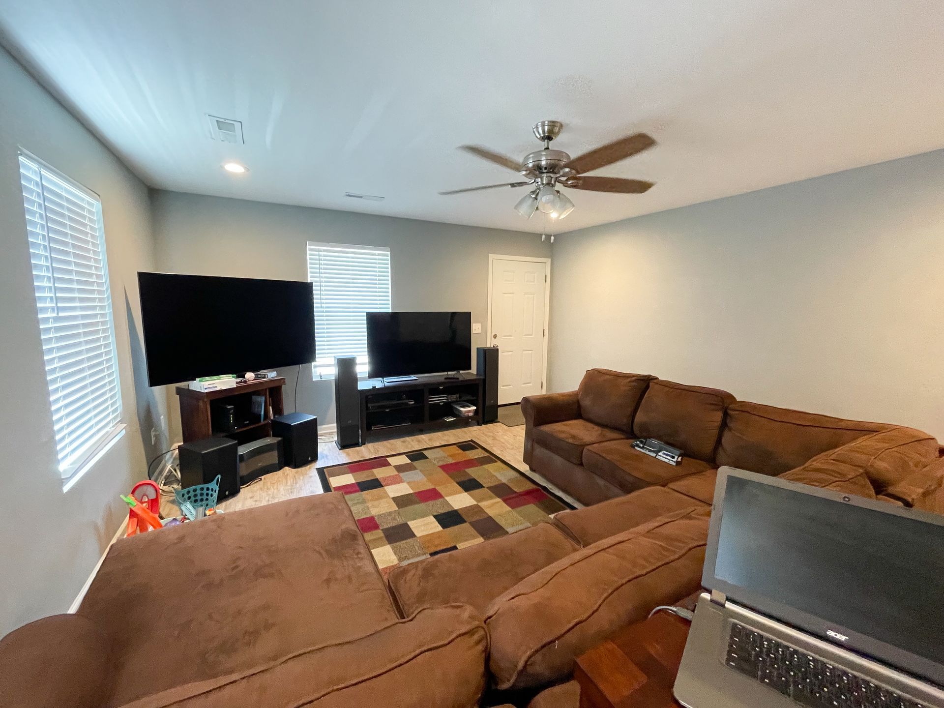 Living room with brown sectional, two TVs, ceiling fan, and patterned rug