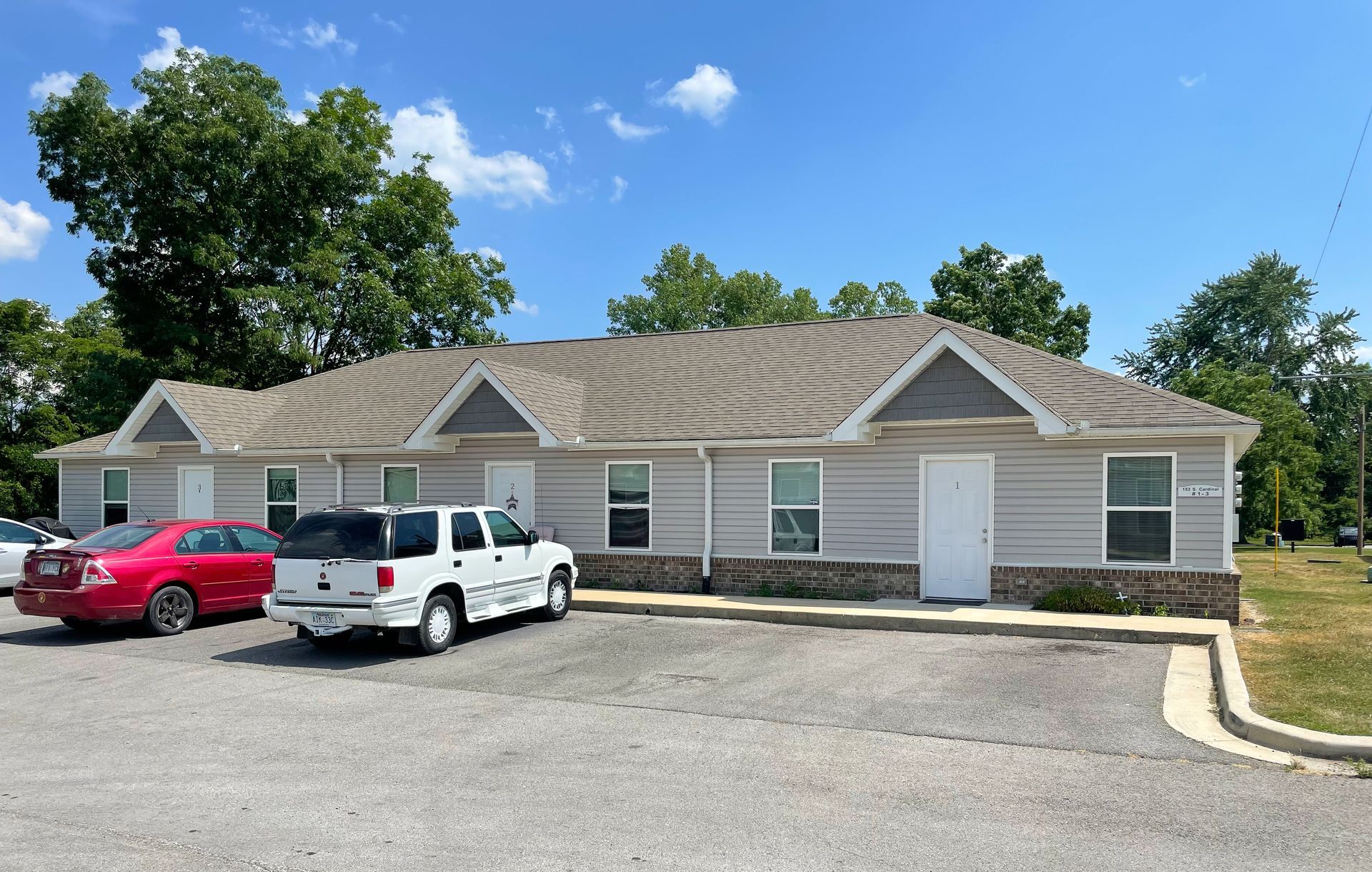 Single-story brick office building with parked red and white vehicles under a blue sky