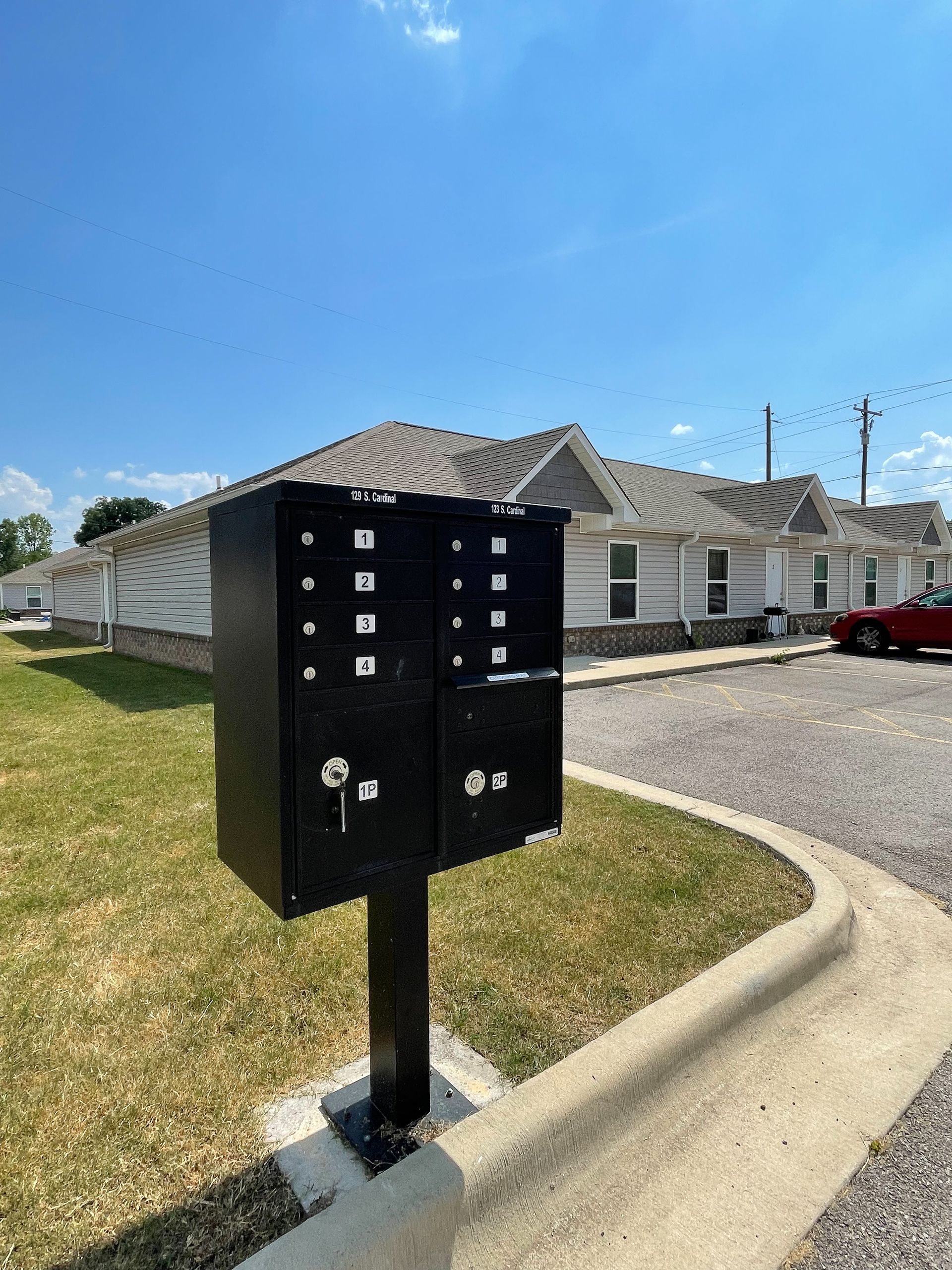 Black outdoor mailbox cluster on a post beside a curb in a suburban apartment complex drive.